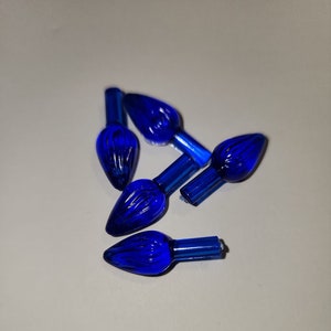 May include: Six blue Christmas light bulbs with a pointed tip and a textured surface.