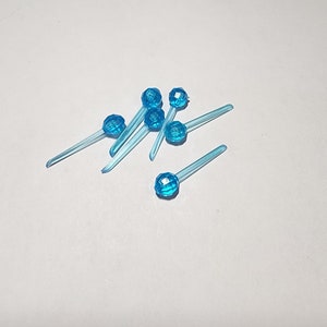 May include: A collection of six light blue Christmas light bulbs with faceted, round tops and long, thin stems. The bulbs are scattered on a white surface, creating a festive and decorative arrangement.
