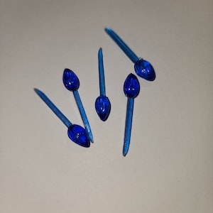 May include: Five blue plastic Christmas tree light bulbs with a pointed tip. The bulbs are on a white surface.