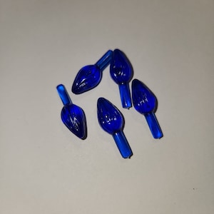 May include: Six blue plastic Christmas light bulb replacements. The bulbs are shaped like a flame and have a textured surface.