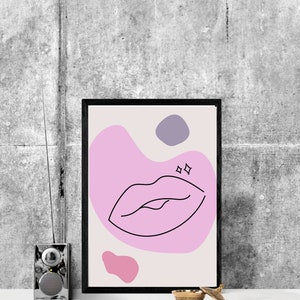 May include: A framed print with a pink and purple abstract design featuring a black line drawing of a pair of lips. The lips are surrounded by a pink blob with two small white stars above them.