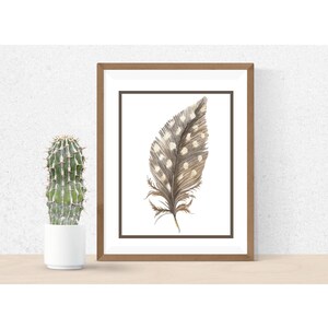 May include: A framed watercolour painting of a brown and white spotted feather with a white background.