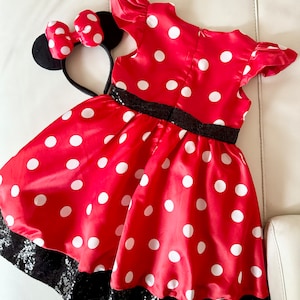 May include: Red polka dot dress with black sequin trim and a matching black headband with red polka dot bow and black mouse ears.