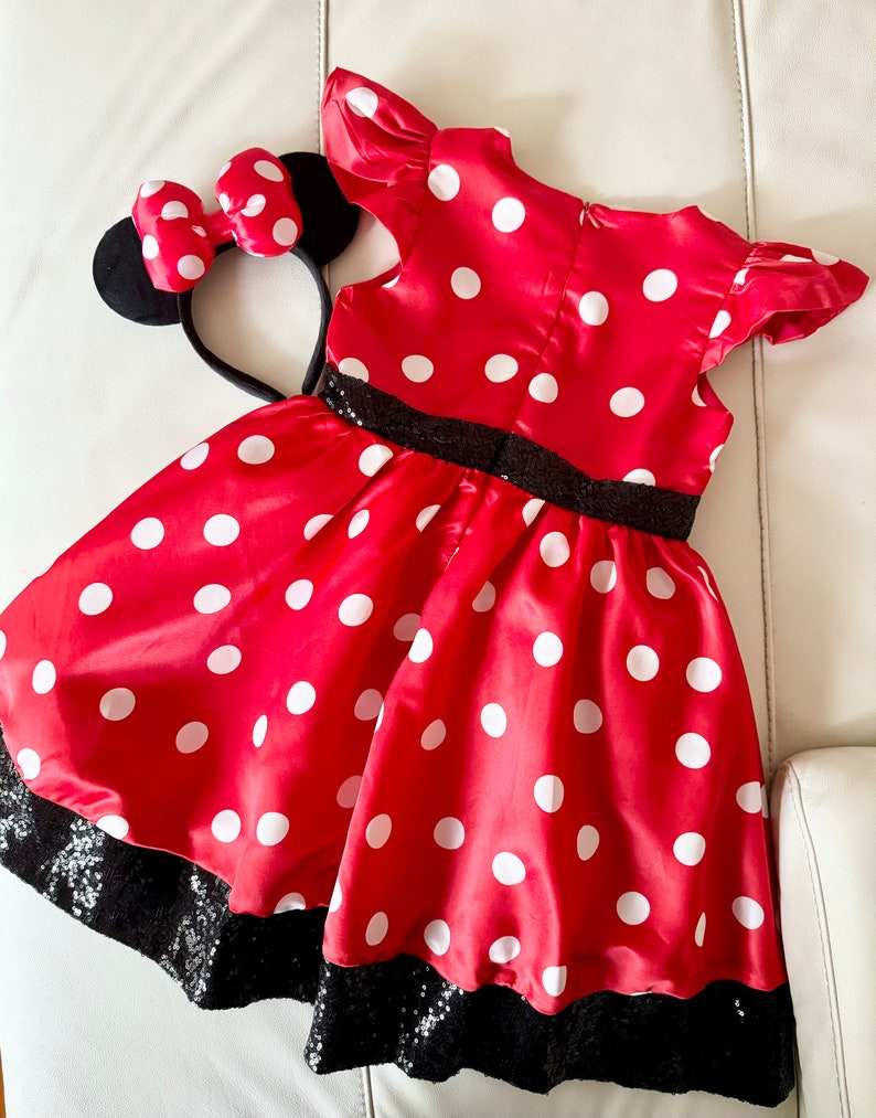 May include: Red polka dot dress with black sequin trim and a matching black headband with red polka dot bow and black mouse ears.