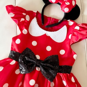 May include: Red polka dot dress with a black sequin bow and a black headband with red polka dot bow and black ears.