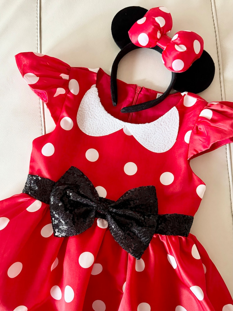 May include: Red polka dot dress with a black sequin bow and a black headband with red polka dot bow and black ears.