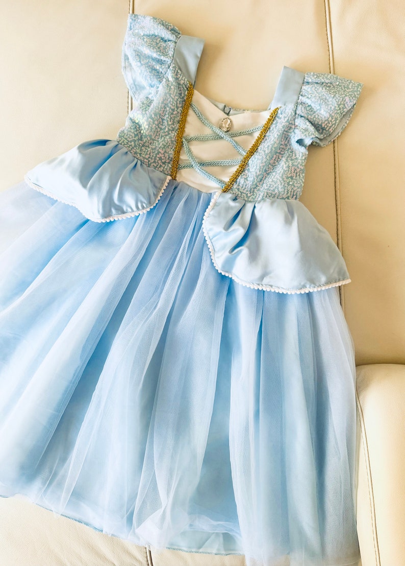 K&ouml;nnte beinhalten: Ein hellblaues T&uuml;llkleid mit einem Satin-Oberteil und goldenen Verzierungen. Das Kleid hat einen Schn&uuml;rr&uuml;cken und einen R&uuml;schenrock.