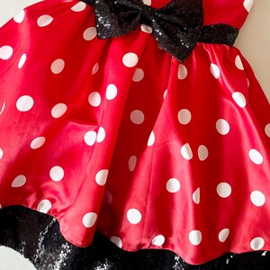 May include: Red dress with white polka dots and a black sequin bow. The dress has a black sequin trim around the bottom.