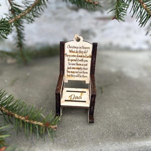 May include: A wooden chair ornament with the text "Christmas in Heaven" and a poem about remembering loved ones. The word "Dad" is inscribed on the chair. The ornament is brown and beige, with a natural wood grain finish.