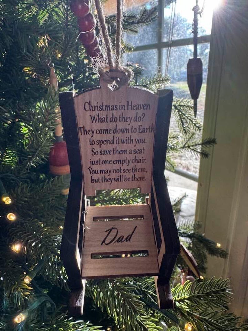 May include: A wooden chair-shaped Christmas ornament with the text "Christmas in Heaven" and "Dad". The ornament is hanging on a Christmas tree. The text on the ornament reads: "They come down to Earth to spend it with you. So save them a seat just one empty chair."