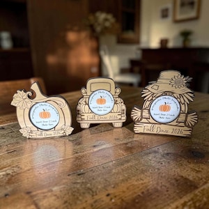 May include: Three light-colored wooden magnetic photo frames with fall themes. One is shaped like a pumpkin, one like a truck, and one like a scarecrow. Each features a circular center with the text "Magnetic Photo Keepsake" and "Fall Daze 2026".