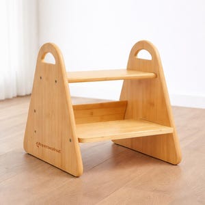 May include: A two-step wooden stool with a natural finish. The stool has a triangular frame with a handle at the top and two steps. The brand name "Greenwalnut" is printed on the side. The stool is designed for children.