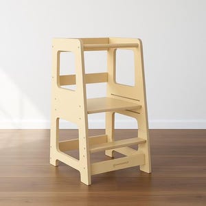 May include: A light-coloured wooden learning tower with a rectangular frame. It has a platform, two steps, and a safety bar. The tower has cut-out handles and is designed to help children reach countertops.