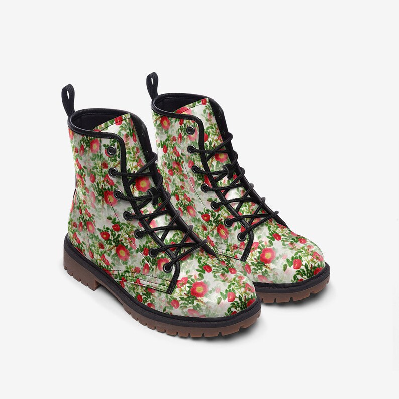 May include: A pair of floral print boots. The boots feature a white background with a pattern of red flowers and green leaves. They have black laces, a black collar, and a brown sole. The boots are designed for everyday wear.