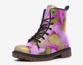 Può includere: Un anfibio con un motivo astratto rosa e oro. Ha lacci neri, un tirante nero e una suola marrone. Questo stivale è una scelta di calzature alla moda e distintiva.