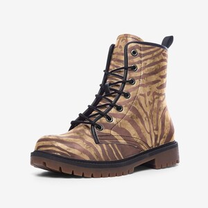 May include: A brown and tan combat boot featuring a zebra stripe design. The boot has black laces, black trim, and a brown lug sole. The boot is made of faux leather.