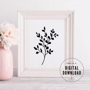 May include: A black and white printable art print of a simple silhouette of a leafy branch in a white frame. The print is sitting on a white wooden surface with a pink vase and white flowers.