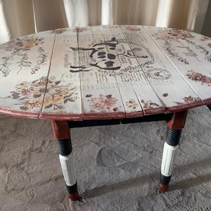 Puede incluir: Una mesa ovalada de hojas caídas blanca con un gráfico de vaca blanco y negro y acentos florales. La mesa tiene patas rojas y negras con acentos blancos.