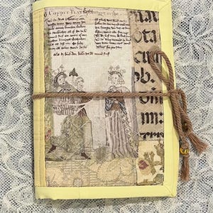 May include: A yellow journal with a brown rope closure and a tassel. The cover is made of fabric with a vintage design featuring a scene of two people in medieval clothing. The text "Copper PLATinting the" is visible on the cover.