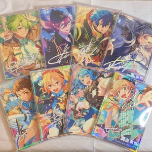May include: A collection of eight holographic cards featuring anime-style characters with colorful backgrounds and signatures. The cards are arranged in a semi-circle on a white surface.