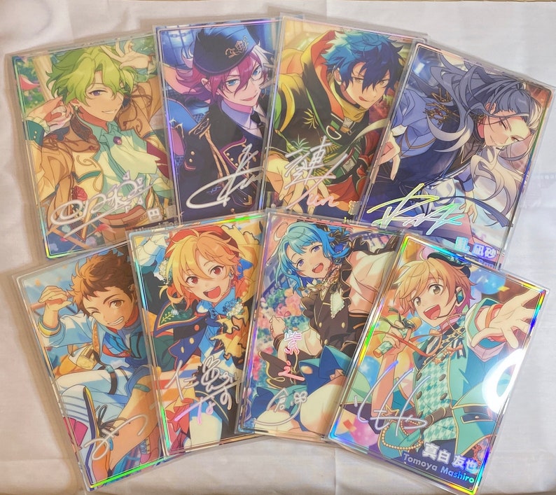 May include: A collection of eight holographic cards featuring anime-style characters with colorful backgrounds and signatures. The cards are arranged in a semi-circle on a white surface.