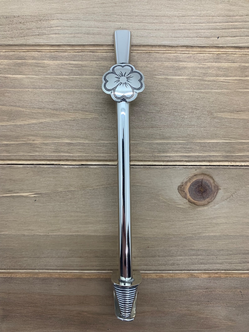 May include: A silver metal straw with a decorative flower design at the top and a spiral design at the bottom.