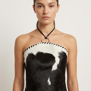 Puede incluir: Top de tubo de piel de vaca en blanco y negro con una correa de cuello halter negra y un detalle de anillo plateado. El top presenta un ribete cosido a lo largo del borde superior. Prenda de vestir única.