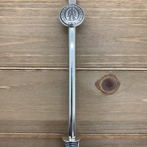 May include: Silver metal straw with a round, decorative top featuring a religious image. The straw has a spring-loaded bottom.