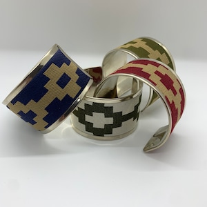 May include: Four silver metal cuff bracelets with different coloured patterned fabric bands. The bands are beige and blue, beige and green, beige and red, and beige and olive green.