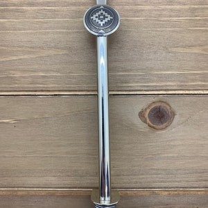 May include: A silver metal stirring stick with a decorative round top featuring a geometric design. The stick has a spiral base.