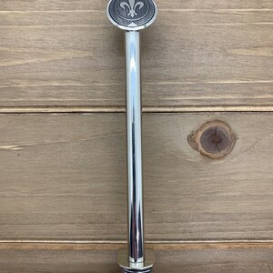 May include: A silver metal pipe with a fleur-de-lis design on the top. The pipe has a spiral design at the bottom.