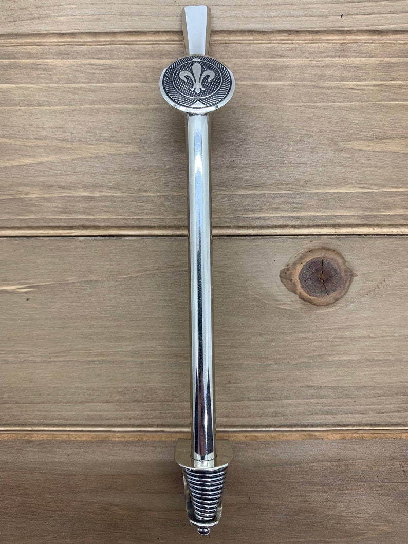 May include: A silver metal pipe with a fleur-de-lis design on the top. The pipe has a spiral design at the bottom.