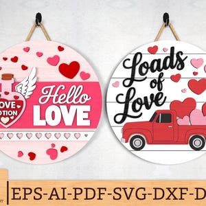 May include: Two round Valentine's Day wooden signs. One features a pink background with a love potion bottle and the words "Hello Love." The other sign has a red truck carrying hearts and the words "Loads of Love."