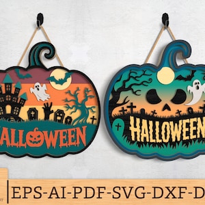 May include: Two pumpkin-shaped Halloween signs made of wood. One is teal, the other black, both with a layered design. Each features a haunted house, ghost, and the word "HALLOWEEN". They hang from a black hook with a beige string.