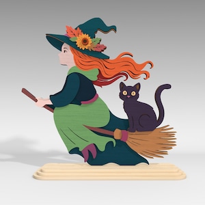 Pu&ograve; includere: Decorazione di Halloween in legno raffigurante una strega su una scopa con un gatto nero. La strega ha i capelli arancioni, un vestito verde e un cappello con fiori. La scopa &egrave; marrone e il gatto &egrave; nero. La decorazione &egrave; su una base chiara.