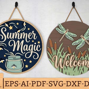 以下が含まれることがあります： ロープハンガー付きの丸い木製サインが2つ。1つは、ホタルと瓶で「Summer Magic」という言葉が特徴です。もう1つは、トンボとガマで「Welcome」と書かれています。サインは青、茶色、緑、ベージュの色合いです。