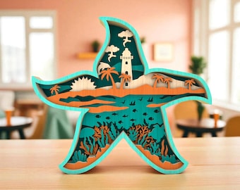 May include: A multi-layered wooden starfish sculpture with a coastal scene. The sculpture features a turquoise frame, with a beach, lighthouse, and ocean design in shades of orange, teal, and natural wood. The sculpture is approximately 10 inches tall.