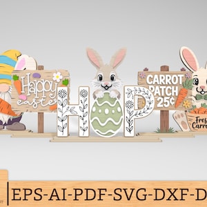 Op de afbeelding: Houten paasdecoraties met een kabouter met een wortel, een konijn met een ei en een konijn met een mandje wortels. De decoraties bevatten borden met de tekst "Happy Easter" en "Carrot Patch 25¢".