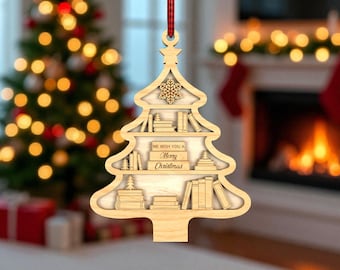 Peut inclure: Ornement de Noël en bois en forme d'arbre avec un design d'étagère. L'ornement présente des étagères avec des livres et le texte "WE WISH YOU A Merry Christmas". Un flocon de neige et une étoile sont en haut. Un ruban rouge et noir est attaché.