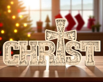 May include: A wooden Christmas decoration spelling out the word "CHRIST". The letters are cut out with detailed nativity scenes and a cross. The decoration is light-colored and sits on a wooden surface.