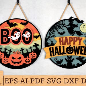 Könnte beinhalten: Zwei runde Halloween-Schilder. Eines zeigt "BOO" mit Geistern und Kürbissen. Das andere zeigt "HAPPY HALLOWEEN" mit einer Hexe, Katze und einem Geist. Beide Schilder sind schwarz, orange und gelb, mit einem Seil zum Aufhängen.