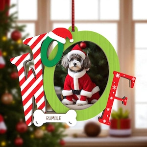 May include: A Christmas ornament with the word "HOPE" in red and white striped letters and green letters. The "O" frames a photo of a dog in a Santa suit. A bone-shaped tag reads "RUMBLE".