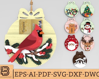 Könnte beinhalten: Weihnachtsschmuck aus Holz mit einem roten Kardinal auf einem verschneiten Ast, der eine Kreditkarte hält. Zusätzliche Ornamente zeigen festliche Designs wie einen Weihnachtsbaum, den Weihnachtsmann und ein Rentier. Das Ornament ist für eine Kreditkarte konzipiert.