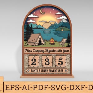 May include: Wooden camping-themed countdown calendar with a scenic landscape of a lake, mountains, and a tent. The calendar displays the numbers 235, with the text "Trips Camping Together this Year" and "Zanta & Jenny Adventures".