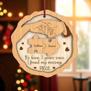 May include: Wooden ornament with a light brown border and a white interior. The ornament features a drawing of two hands holding each other, two puzzle pieces with the names "William" and "Jessica", and the text "It's been 3 years since I found my missing PIECE."