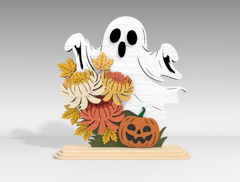 Pu&ograve; includere: Decorazione di Halloween in legno con un fantasma bianco con occhi e bocca neri, accompagnato da fiori arancioni e gialli, una zucca intagliata e foglie verdi. La decorazione &egrave; posta su una base di legno.