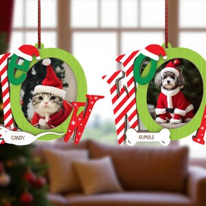 May include: Two Christmas ornaments with the word "MEOW" in red and white stripes and green. One ornament features a cat in a Santa suit, the other a dog in a Santa suit. The cat's name is "Candy" and the dog's name is "Rumble".