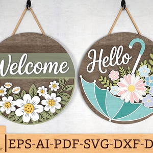 Può includere: Due cartelli rotondi in legno con ganci in corda. Uno dice "Welcome" con margherite bianche. L'altro dice "Hello" con un ombrello e fiori. I cartelli hanno uno stile rustico e country.