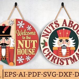 May include: Two circular wooden Christmas decorations. One displays a nutcracker with the words "Welcome to the NUT HOUSE". The other shows a nutcracker and the text "NUTS ABOUT CHRISTMAS". Both signs are red, white, and beige.
