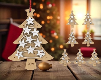 May include: Wooden Christmas tree ornament with star cutouts and personalized names. The ornament is light brown with white stars and a red and black ribbon. The year 2024 is printed on the tree. Additional wooden tree ornaments are also visible.